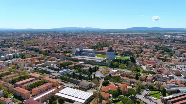 Cinematic aerial footage of Pisa&rsquo;s Piazza&nbsp;dei&nbsp;Miracoli, showcasing the Leaning Tower, Duomo and Baptistery surrounded by terracotta rooftops, lush green lawns and distant Tuscan hills under blue skies
