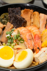 A hearty bowl of seafood noodle soup filled with shrimp, corn, egg, vegetables, rice blood cake, tofu skin, and assorted hotpot ingredients. The colorful ingredients float in a rich broth, making for 