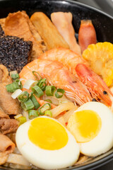 A hearty bowl of seafood noodle soup filled with shrimp, corn, egg, vegetables, rice blood cake, tofu skin, and assorted hotpot ingredients. The colorful ingredients float in a rich broth, making for 