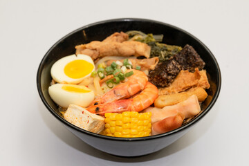 A hearty bowl of seafood noodle soup filled with shrimp, corn, egg, vegetables, rice blood cake,...