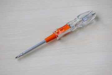 Electric voltage tester with star and flat screwdriver tips. Multi-tester for 100-500V. Professional voltage test driver on a wooden background. Essential electrical tool.