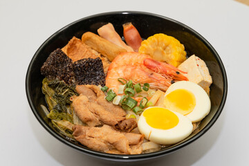 A hearty bowl of seafood noodle soup filled with shrimp, corn, egg, vegetables, rice blood cake, tofu skin, and assorted hotpot ingredients. The colorful ingredients float in a rich broth, making for 