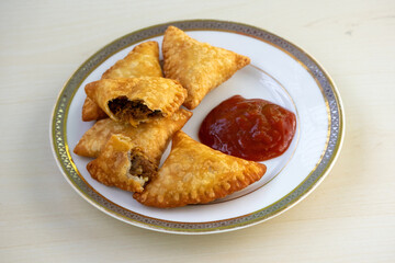 Plate of Delicious Beef Samosas with Tomato Sauce. Popular Crispy Snack Food in Bangladesh, Pakistan, India. Also known as Samsa, Sambosas, Sambusak, Sanbusak, Sanbusaq, Sanbusaj, Samoosa.