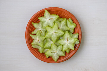 Top view of vibrant sliced star fruit (Averrhoa carambola), known as Kamranga in Bengali, arranged beautifully on a rustic clay plate. Fresh, juicy, and ready for your designs.