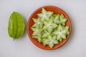 Vibrant, freshly sliced star fruit (Averrhoa carambola), known as Kamranga in Bengali, artfully arranged on a rustic clay plate. Captivating top view for your projects.