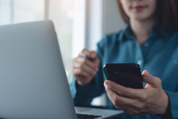 Business woman using mobile smart phone and working on laptop computer at office. Woman online...