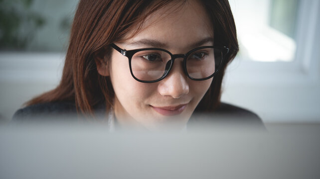 Closeup, asian business woman with eyeglasses working on computer, looking at the computer monitor screen at office