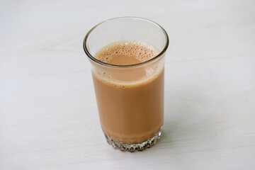 Delicious hot milk tea with frothy bubbles in a clear glass cup on a light wooden table, perfect for cozy drink photography and beverage concepts.