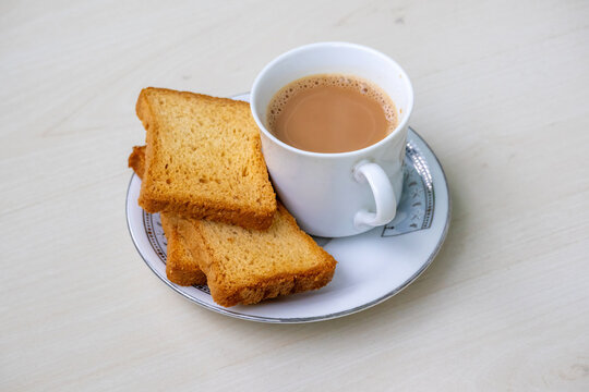 Steaming hot milk tea with delightful bubbles and crunchy rusk biscuits artfully arranged on a wooden backdrop. This inviting drink, known as dudh cha or doodh cha, is ideal for cozy moments.