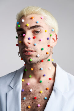 Trendy young man with multicolored pellets on face and neck looking at camera against gray background