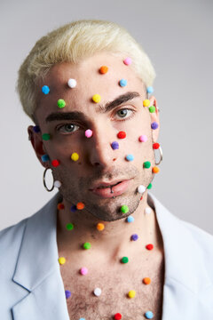 Trendy young man with multicolored pellets on face and neck looking at camera against gray background