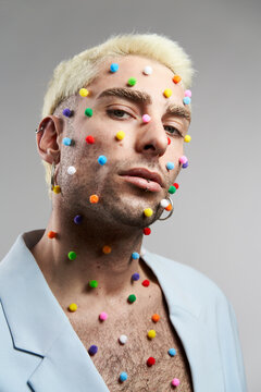 Trendy young man with multicolored pellets on face and neck looking at camera against gray background