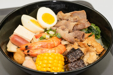 A hearty bowl of seafood noodle soup filled with shrimp, corn, egg, vegetables, rice blood cake, tofu skin, and assorted hotpot ingredients. The colorful ingredients float in a rich broth, making for 