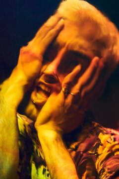 Distorted reflection of anxious young man touching head and screaming on dichroic film