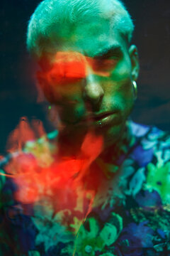 Young male with dyed hair and piercing looking at camera through bright dichroic film
