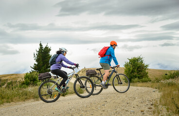 Two people cycling uphill. Man standing up on bike climbing. Otago Central Rail Trail. South...