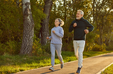 Happy smiling sporty senior couple wearing sportswear jogging in the park having sport workout....