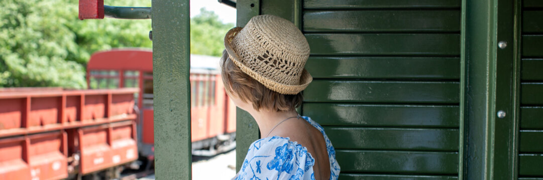 A Caucasian woman in a straw hat gazes from a vintage train, evoking nostalgic railway journeys and Slow Travel Day
