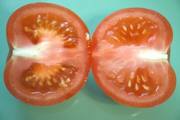 Two halves of a juicy red tomato on a bright blue background. Fresh and simple food composition...