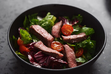 Steak salad with cherry tomatoes and mixed greens in black bowl