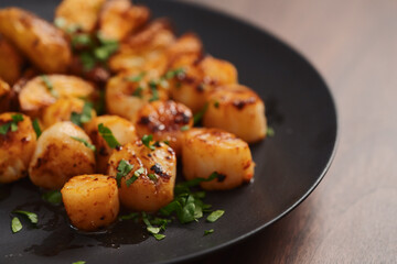roasted scallops with baked potatoes wedges on a black plate on walnut wood background