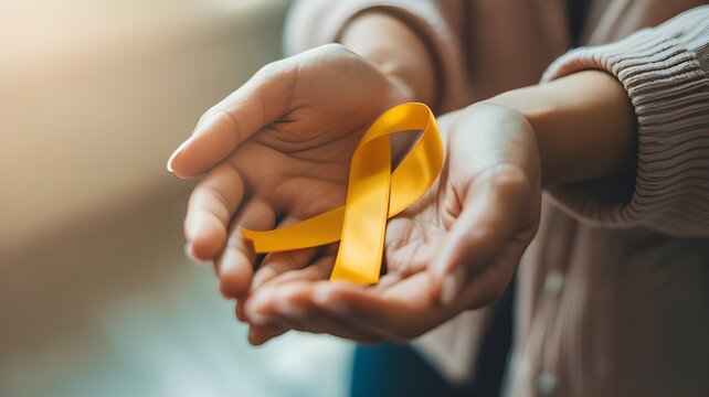 Young female holding yellow gold ribbon awareness symbol for endometriosis, suicide prevention, sarcoma bone cancer, bladder cancer, liver cancer and childhood cancer concept. Health care. Copy space.