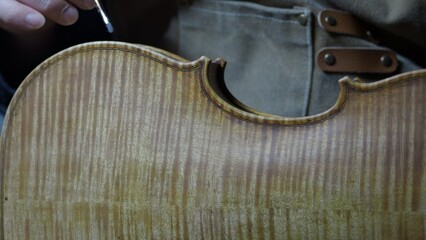 Obraz premium Skilled craftsman applying traditional varnish technique with delicate brush strokes, creating vintage patina on handmade violin surface, enhancing instrument's refined musical character
