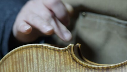 Skilled luthier hand applying protective varnish layer on violin body, carefully working in traditional wooden craftsman workshop with meticulous technique