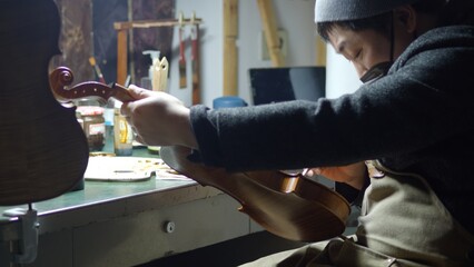 Luthier carefully applying dark varnish to handcrafted violin with soft brush, creating vintage patina in traditional wooden workshop, highlighting meticulous instrument making skill