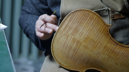 Obraz premium Skilled luthier carefully applying varnish to handcrafted violin, using traditional antiquing technique for enhanced vintage aesthetic and visual depth