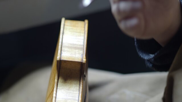 Skilled luthier applying varnish to violin using delicate brush technique, highlighting intricate craftmanship within vintage wooden workshop setting - Powered by Adobe
