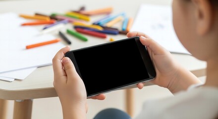 A beautiful photorealistic mockup of a child's hands holding a smartphone with a blank screen, with colorful crayons blurred in the background.