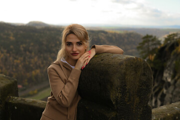 Woman in a beige outfit walking through a natural park with beautiful green cliffs on a cloudy day. Serene moment, connection with nature, stylish outdoor lifestyle.