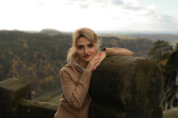 Woman in a beige outfit walking through a natural park with beautiful green cliffs on a cloudy day. Serene moment, connection with nature, stylish outdoor lifestyle.