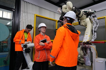 Fototapeta premium group of engineers wearing helmets workshop programming software for automated manufacturing technology and for use in the manufacturing industry and checking the operation and maintenance of the robo