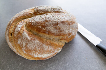 artisan bread with twisted top on gray surface with serrated knife, side view