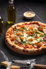 Shrimp and arugula pizza with cheese and tomato sauce on dark stone background