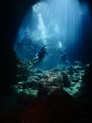 scuba divers in cave coming up to the surface with sun beams and rays