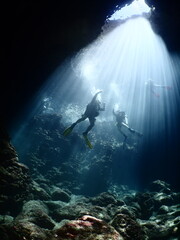 scuba divers in cave coming up to the surface with sun beams and rays