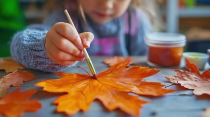 A child paints the veins of a bright orange autumn leaf during an arts and crafts activity
