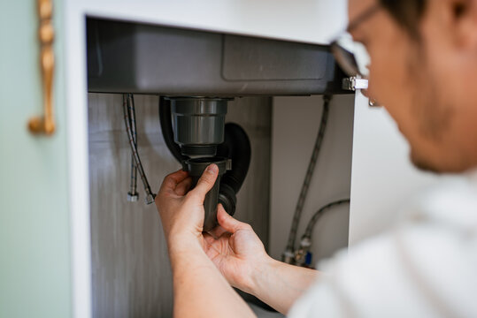 Professional plumber working diligently on installing a siphon beneath the kitchen sink, ensuring effective water drainage while preventing potential leaks and maintaining system integrity