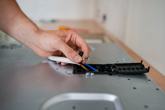 Professional electrician wiring terminal block of electric stove, connecting cables carefully during kitchen renovation process, maintaining electrical safety standards