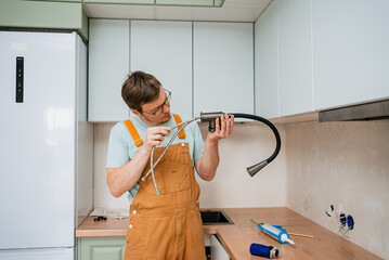 Professional plumber carefully connecting flexible hoses to new kitchen faucet, ensuring proper...