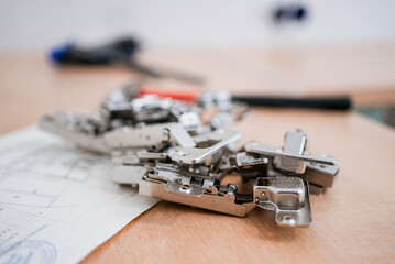 Many furniture hinges are lying on top of a kitchen project on a wooden worktop, ready for use in...