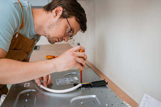 Professional electrician connecting wires and using a screwdriver while installing a new electric stove in a contemporary kitchen, showcasing expertise in appliance installation