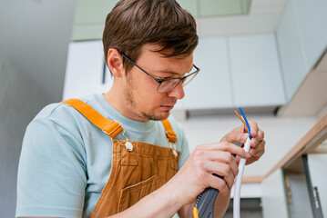 Skilled electrician stripping wire insulation with precision tool, connecting electric stove during...