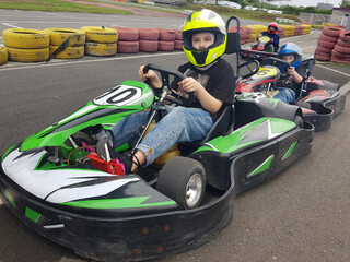 A cute child wearing a yellow helmet enjoying a thrilling ride on a karting track with other kids...