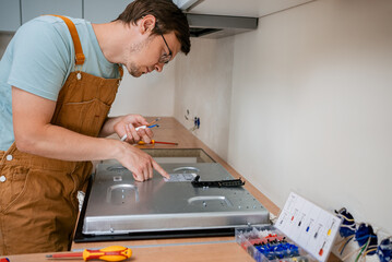 Electrician carefully connects cables to a new electric stove, ensuring proper installation and...