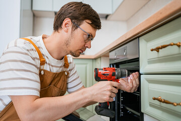 Skilled handyman is meticulously installing a modern oven into a contemporary kitchen cabinet using...