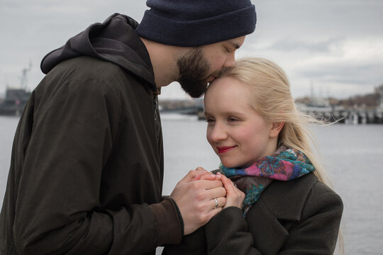 Bearded man and young blond woman couple hugging each other kissing at seaside
